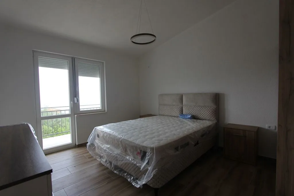 A bedroom featuring a new double bed with plastic wrap and balcony access.