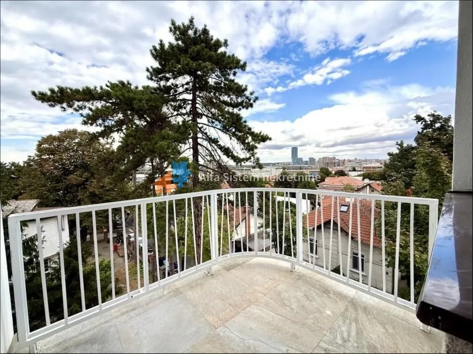 Balkon sa belom ogradom i pogledom na grad i drveće.