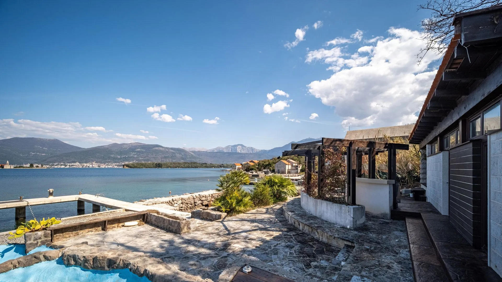 Eksterijer nekretnine sa popločanim dvorištem, terasom i pogledom na more i planine.