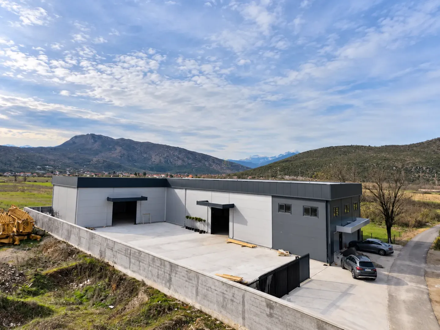 Aerial view of a newly built commercial warehouse building with a yard and mountain landscape in the background.