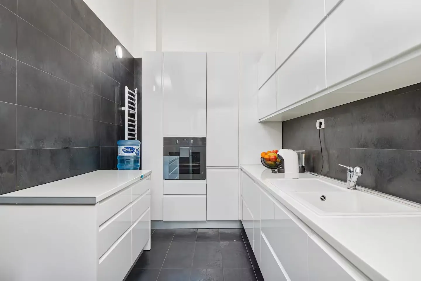 Modern white kitchen with dark wall tiles and built-in appliances.