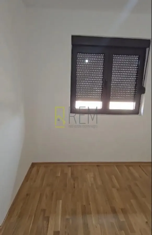Prazna soba sa parketom i prozorom sa roletnama.