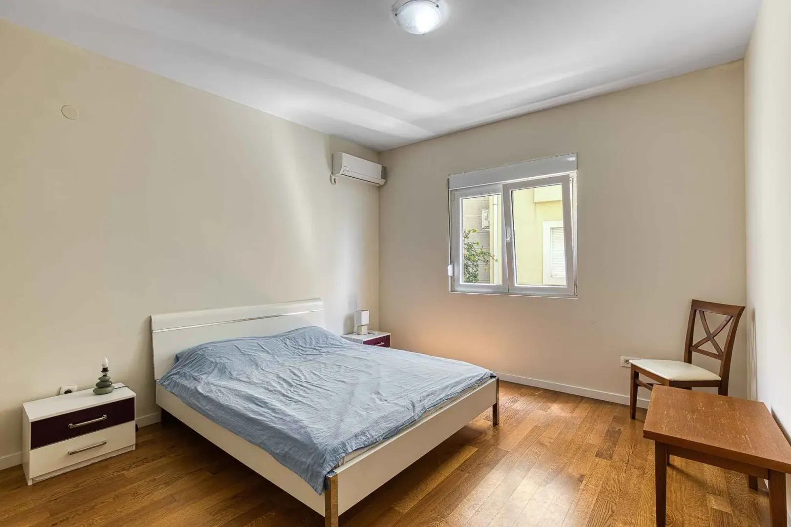 Namještena spavaća soba sa bračnim krevetom, noćnim stočićima i drvenim podom.