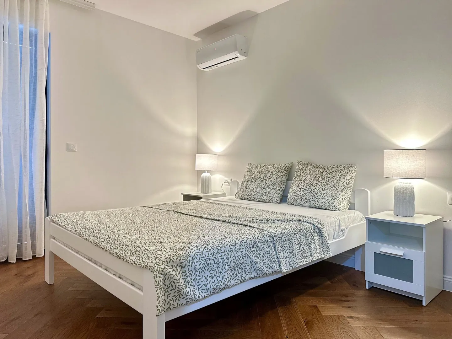 Modern bedroom with a double bed, bedside tables, and an air conditioner.