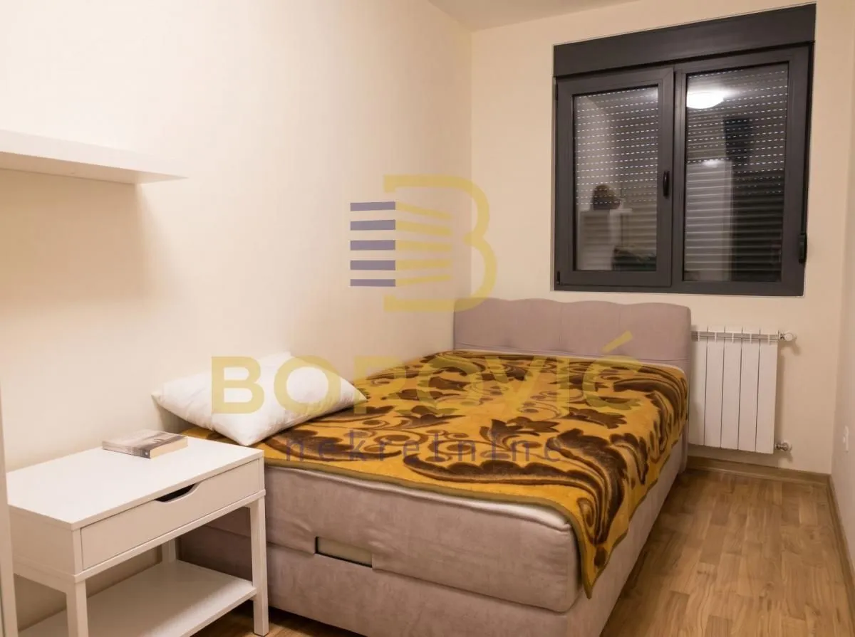 Nameštena spavaća soba sa krevetom i belim noćnim stočićem.