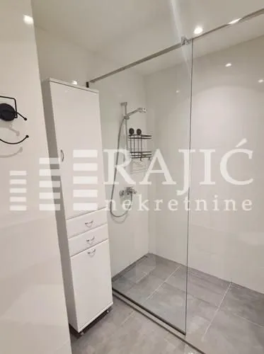 Modern bathroom with walk-in shower and white furniture.