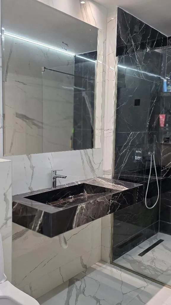 Modern bathroom with marble tiles, washbasin and shower enclosure.