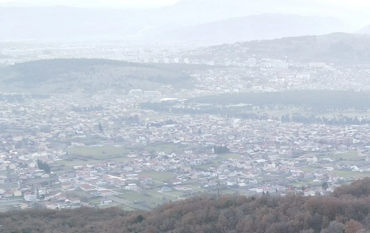 Panoramski pogled na naselje i okolna brda pod maglom.