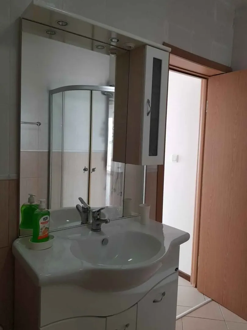 Kupatilo sa umivaonikom, ogledalom i tuš kabinom u odrazu.