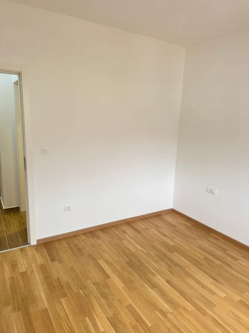 Empty room with white walls and wooden parquet flooring.