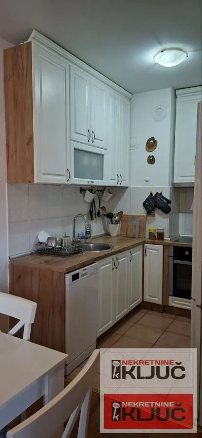 Manja kuhinja sa belim elementima, drvenom radnom pločom i ugrađenim kućnim aparatima.