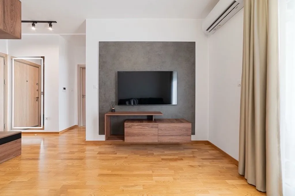 Moderan dnevni boravak sa drvenim podom, televizorom na zidu i klima uređajem.