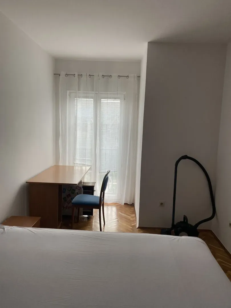 A simple bedroom with a desk, chair, and access to a balcony.