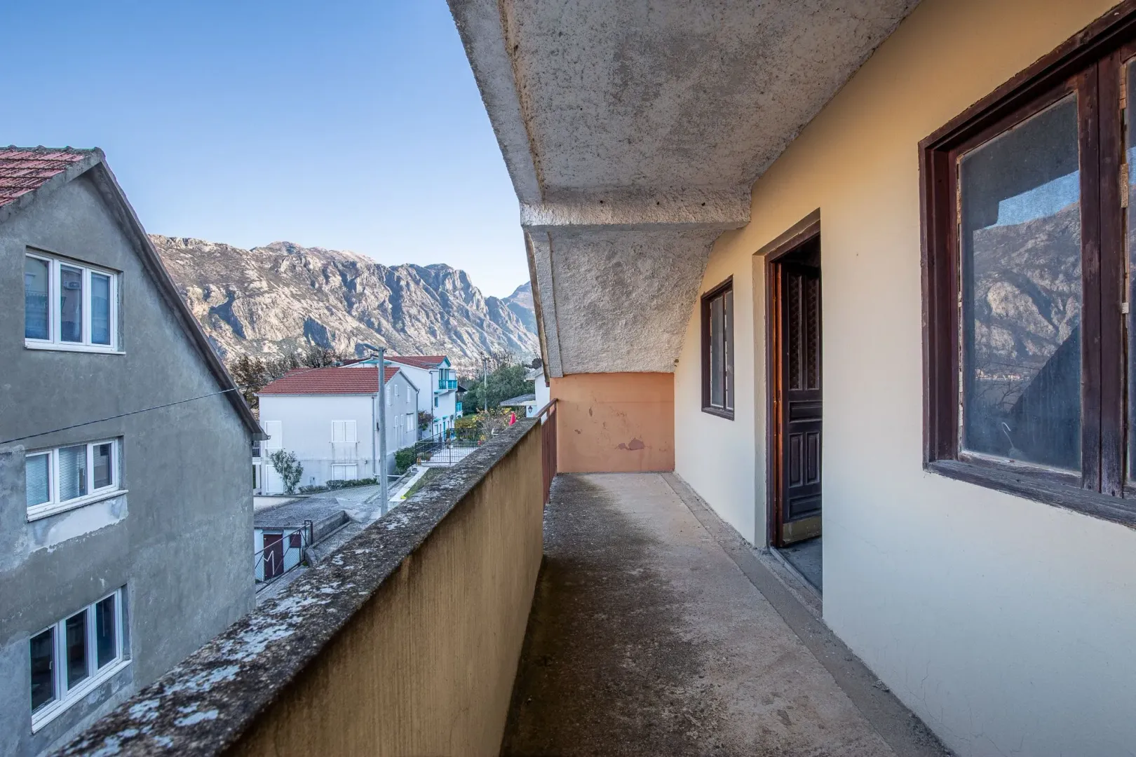 Dugački spoljni balkon sa pogledom na okolne kuće i planine.