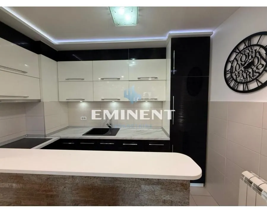 Moderna kuhinja sa belim i tamnim elementima i šankom.