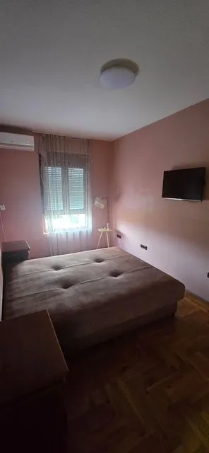 Spavaća soba sa bračnim krevetom, televizorom i prozorom.