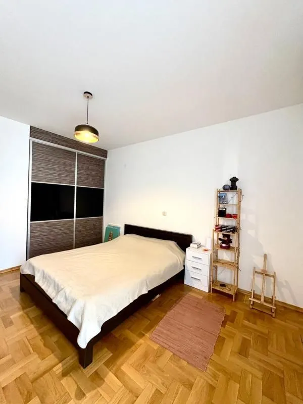 Spavaća soba sa bračnim krevetom, plakarom i drvenim podom.