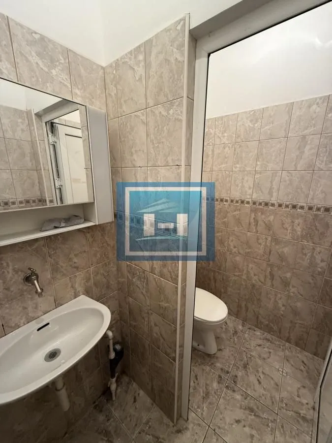 Manje kupatilo obloženo keramičkim pločicama sa umivaonikom, ogledalom i wc šoljom.
