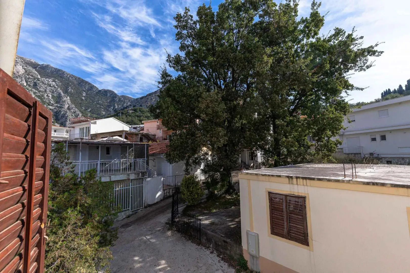 Pogled izbliza na dvorište i okolne kuće sa drvećem.