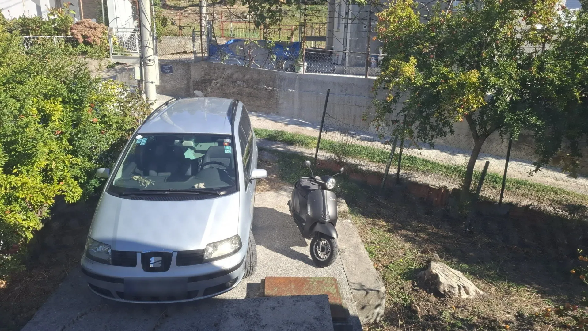 Pogled na dvorište i parking ispred kuće sa automobilom i skuterom.