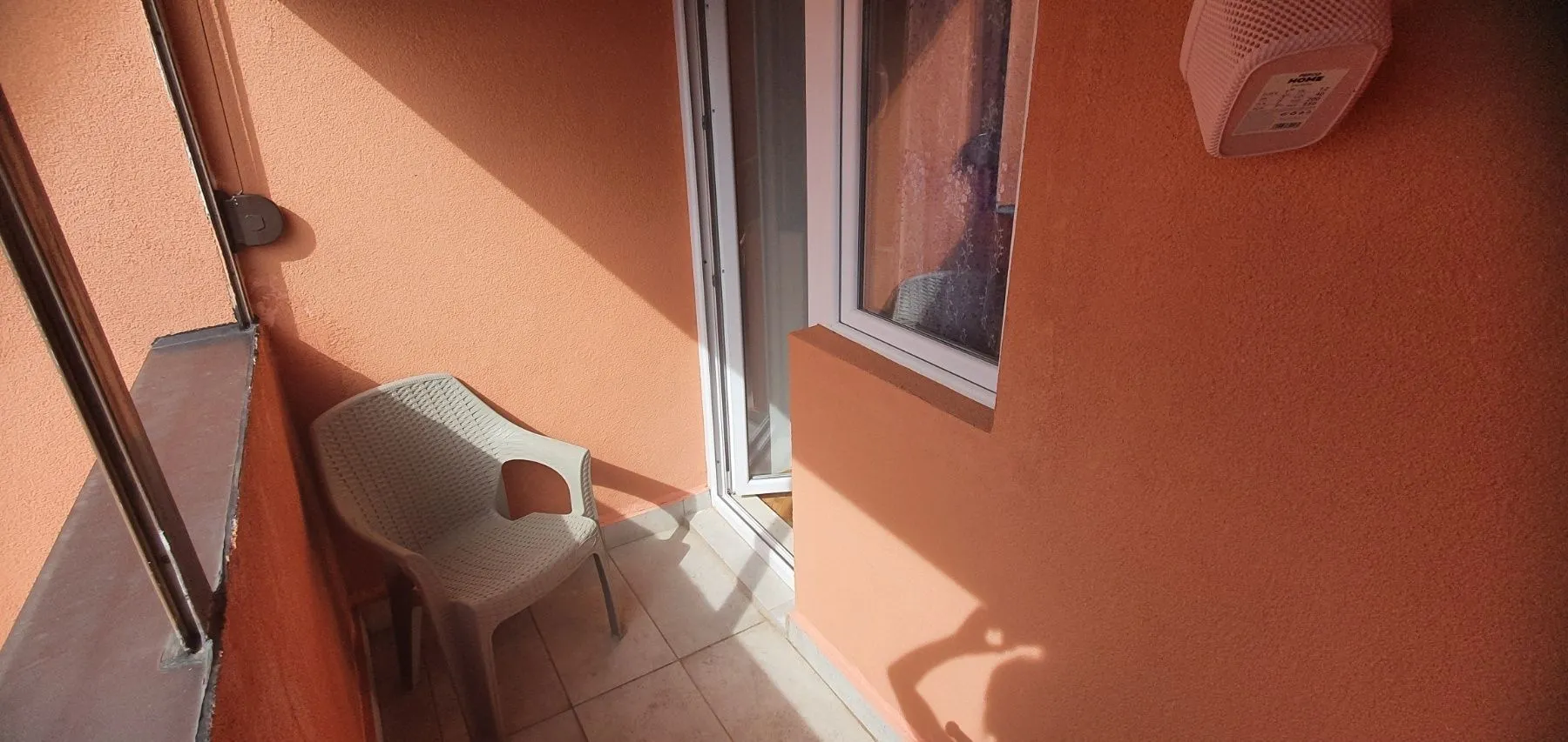 Mali balkon sa jednom plastičnom stolicom i narandžastim zidovima.