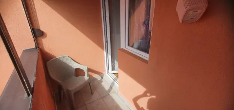 Mali balkon sa jednom plastičnom stolicom i narandžastim zidovima. - image 10