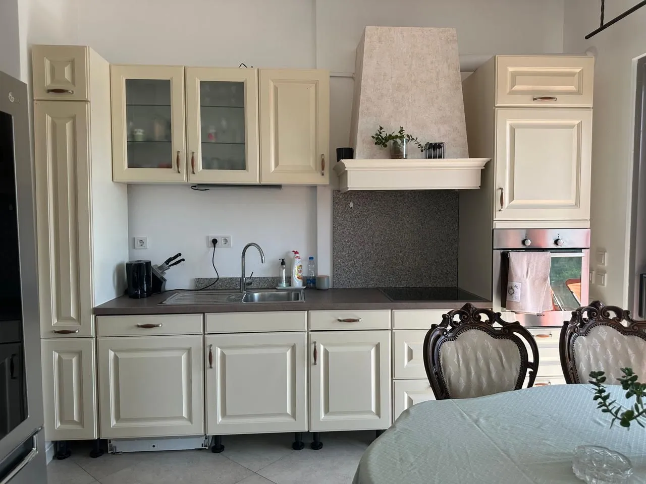 Bright-toned kitchen with built-in appliances and a dining table in the foreground.