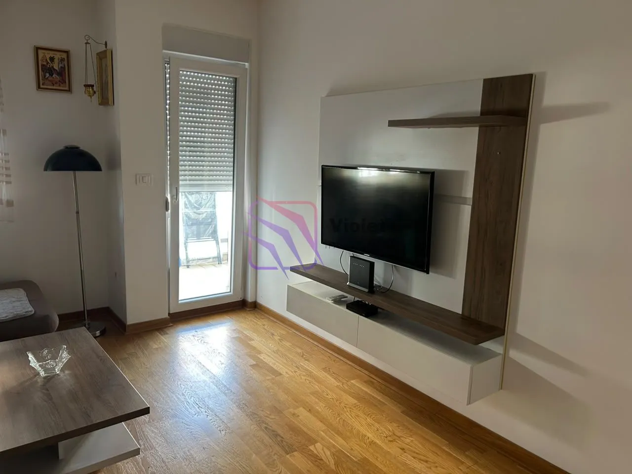 Dnevna soba sa TV elementom, drvenim podom i izlazom na terasu.