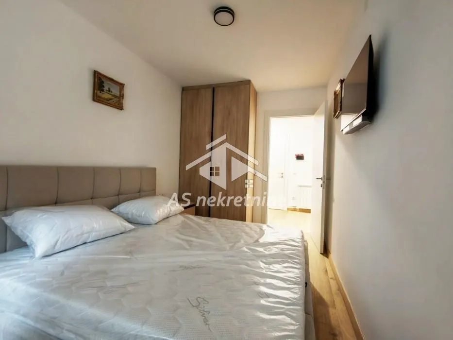 Furnished bedroom with a double bed, wardrobe, and wall-mounted television.
