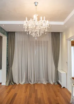 Decorated living room with wooden flooring, a large window with curtains, and a crystal chandelier. - image 5