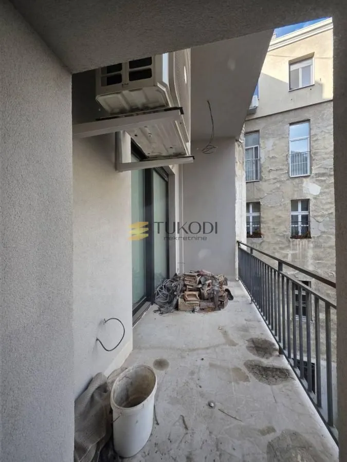 Nenamešten balkon sa klima-uređajem i pogledom na susednu zgradu.