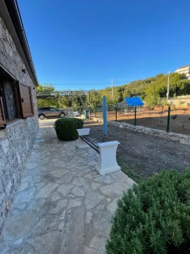 Popločano dvorište sa klupom pored kamene kuće. - image 20