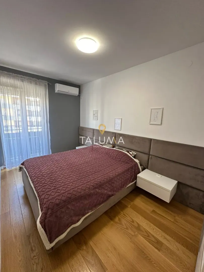 Spavaća soba sa bračnim krevetom, drvenim podom i izlazom na balkon.