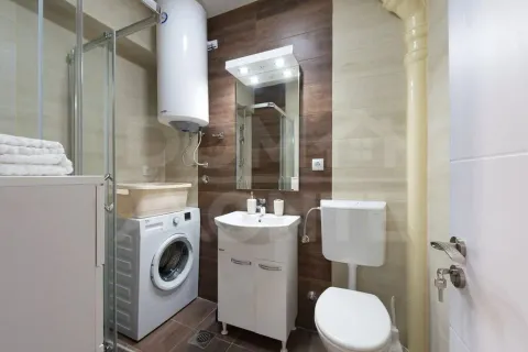 Small bathroom with a shower cabin, washbasin, toilet, and washing machine. - image 13