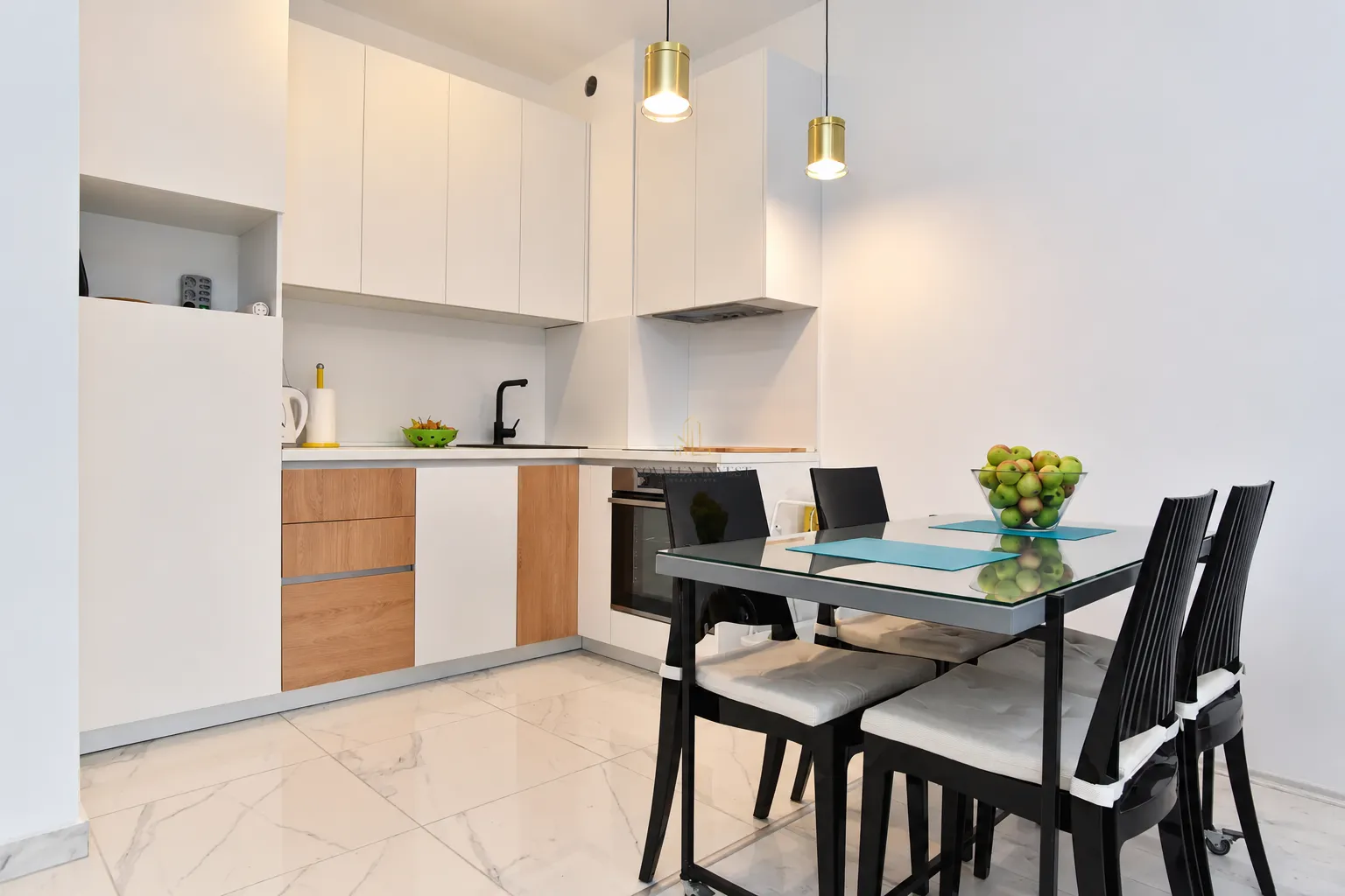 Modern kitchen with white cabinetry, built-in appliances, and a dining table with black chairs.