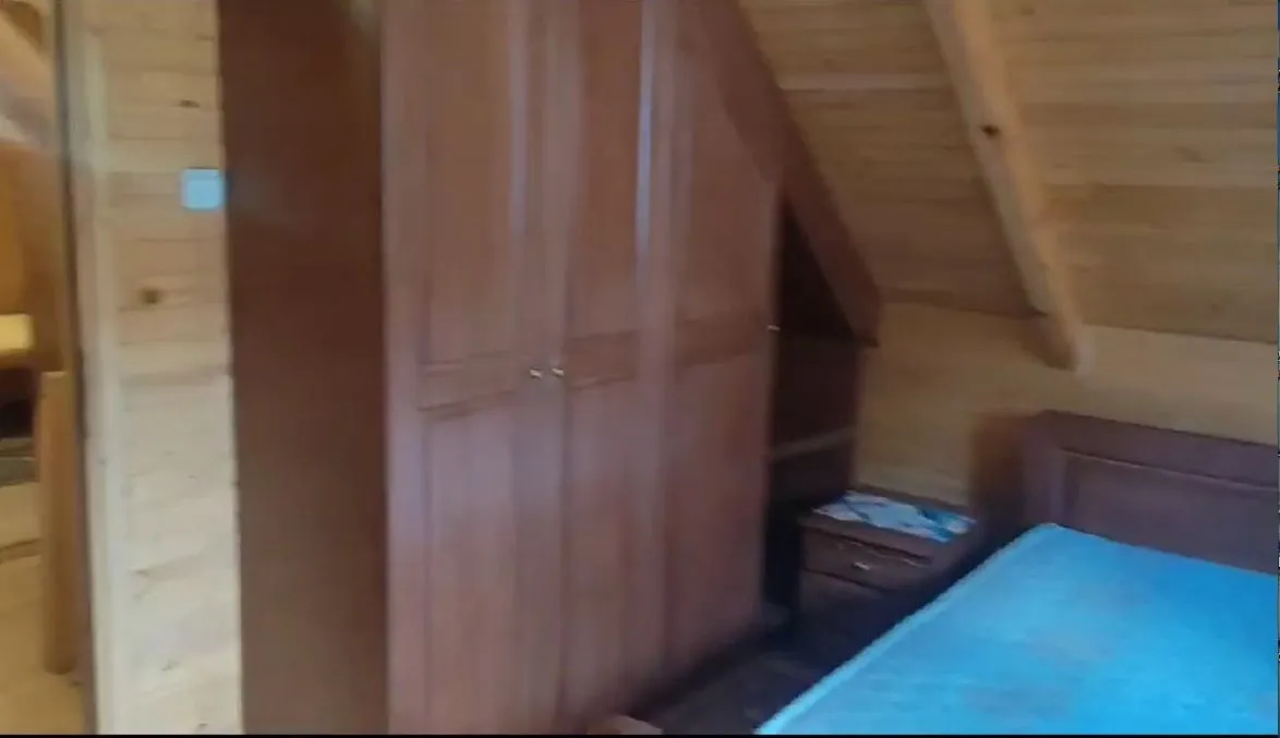 Spavaća soba u drvenoj kućici sa krevetom i ormarom.