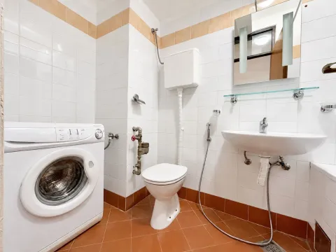 Small bathroom with white tiles, washbasin, toilet, and washing machine. - image 10