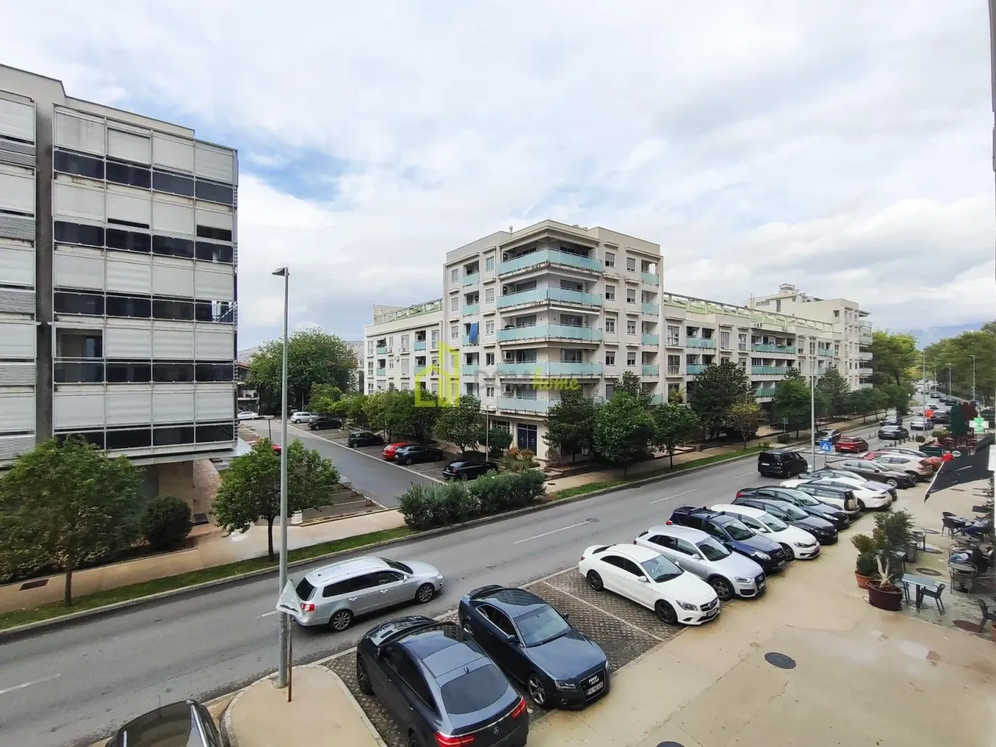 View from the window of a street with parked cars and residential buildings.