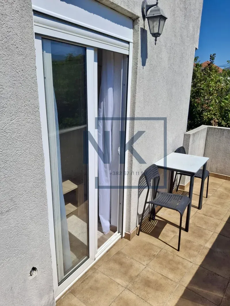 Small tiled balcony with a table and two chairs next to the balcony door.