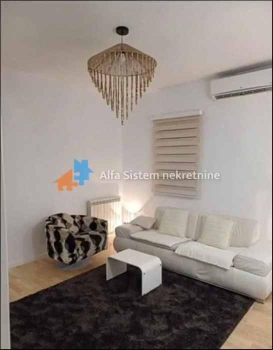 Dnevna soba sa garniturom, foteljom i dekorativnim lusterom.