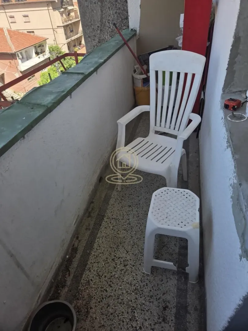 Manji balkon sa plastičnim stolom i stolicom i pogledom na okolne zgrade.