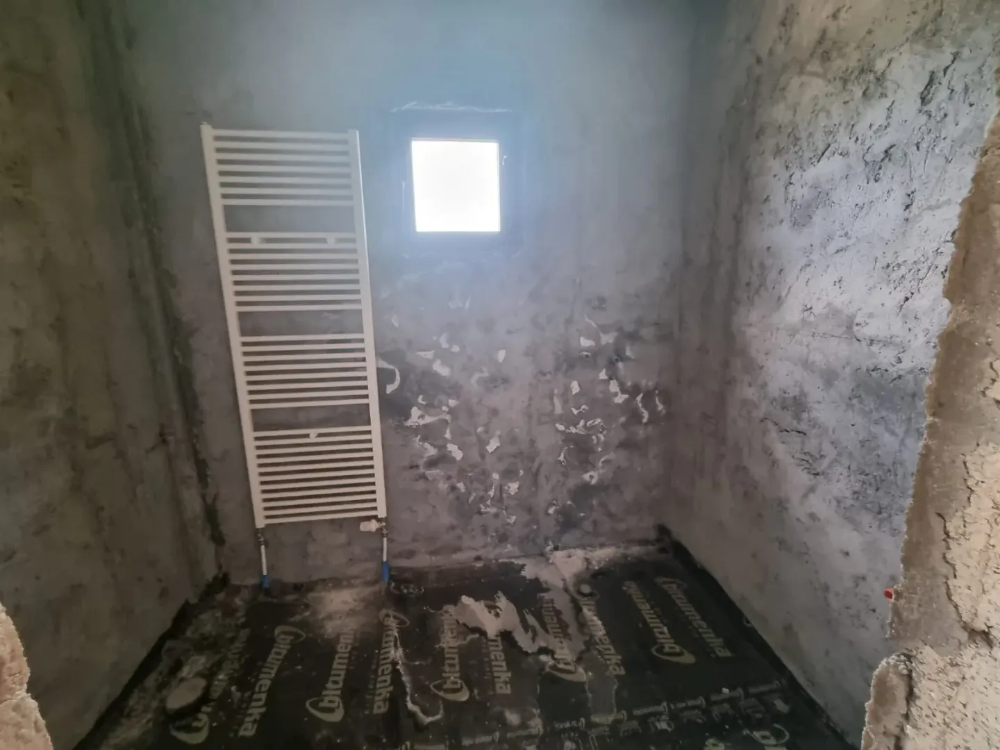 Prostorija u sivoj fazi gradnje sa instaliranim zidnim radijatorom.