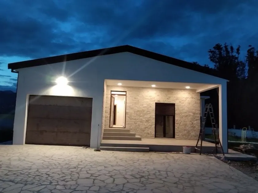 Exterior of a single-story house with a paved yard and garage at dusk.
