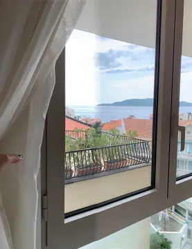 Pogled na more i okolne zgrade kroz prozor. - image 11