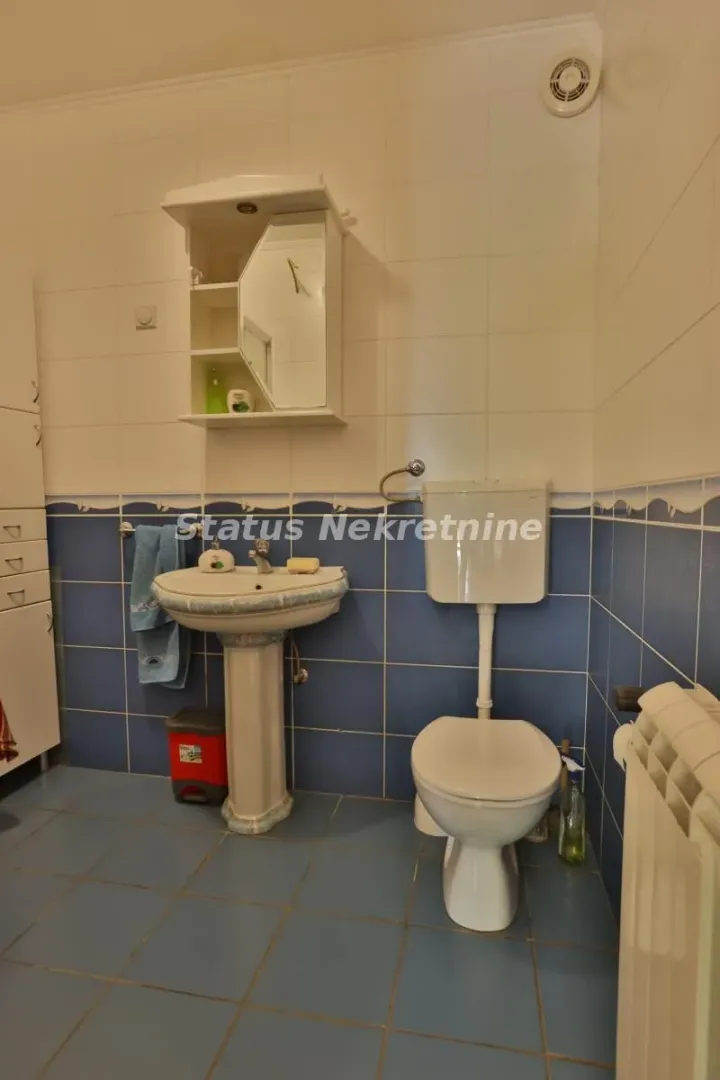 Kupatilo opremljeno umivaonikom, WC šoljom i zidnim ormarićem sa ogledalom.