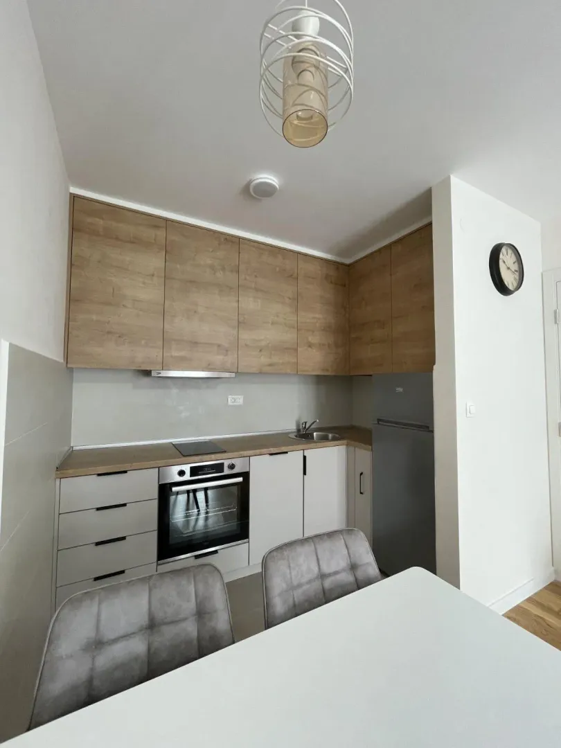 Small kitchen with wooden cabinets, built-in appliances and a dining table in the foreground.
