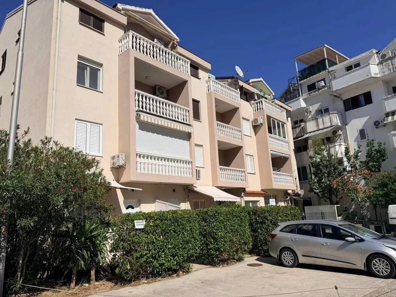 Exterior of an apartment building with a balcony and parking in front.