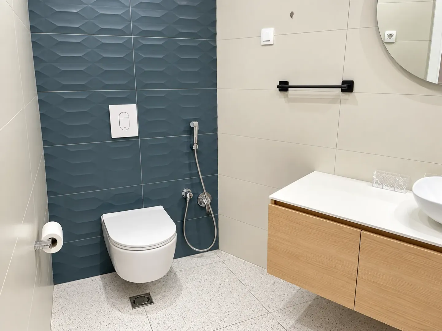 Modernly equipped bathroom with a toilet, bidet spray, and sink.