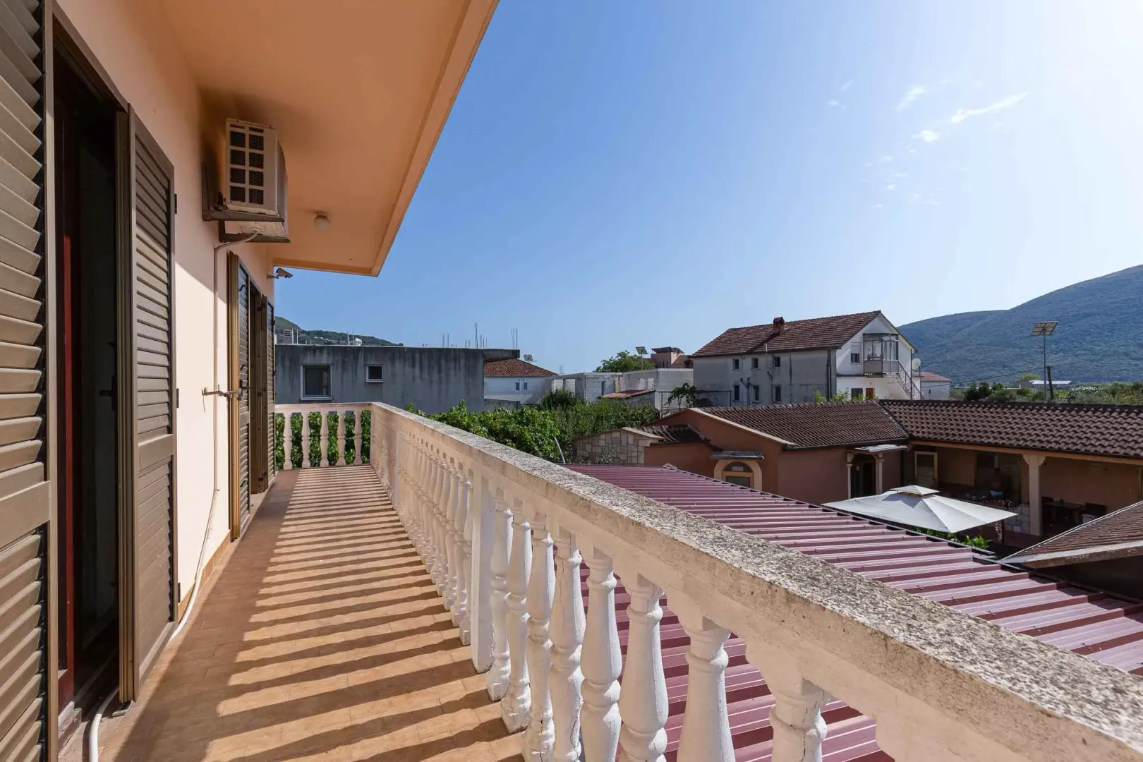 Dugački balkon sa bijelom kamenom ogradom i pogledom na okolne zgrade i brda.