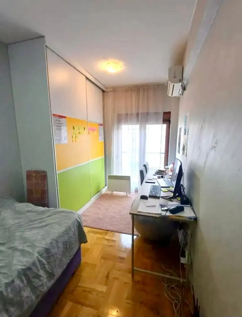 Manja spavaća soba sa krevetom, radnim stolom i garderoberom.